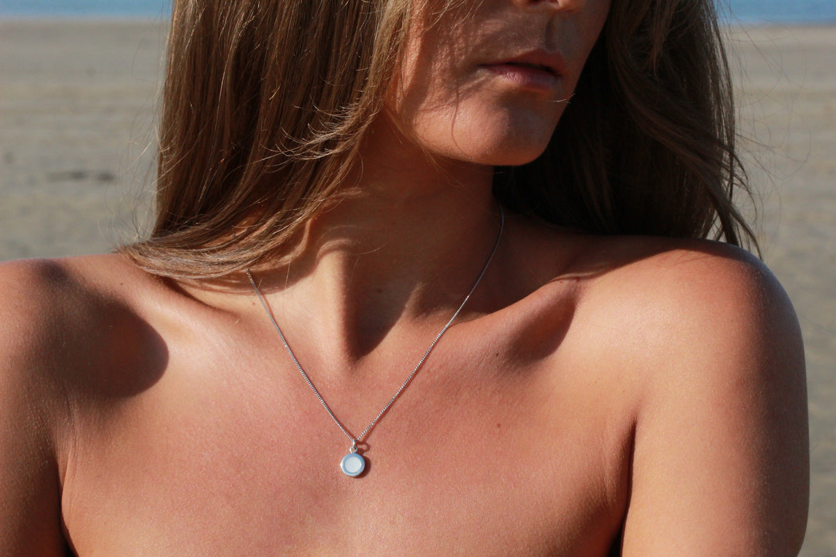 Woman on the beach in the sun wearing a silver-colored Circle of Life round breast milk pendant