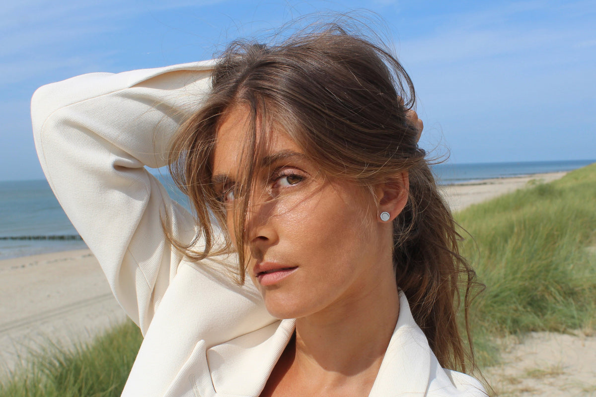 Woman on a beach with her arm raised, wearing a silver Circle of Life breast milk stud earring