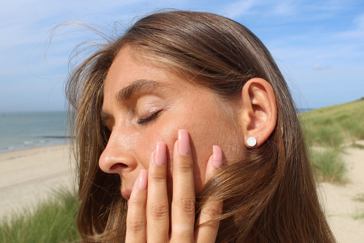 Woman with eyes closed and hand on her cheek, wearing a silver Circle of Life breast milk stud