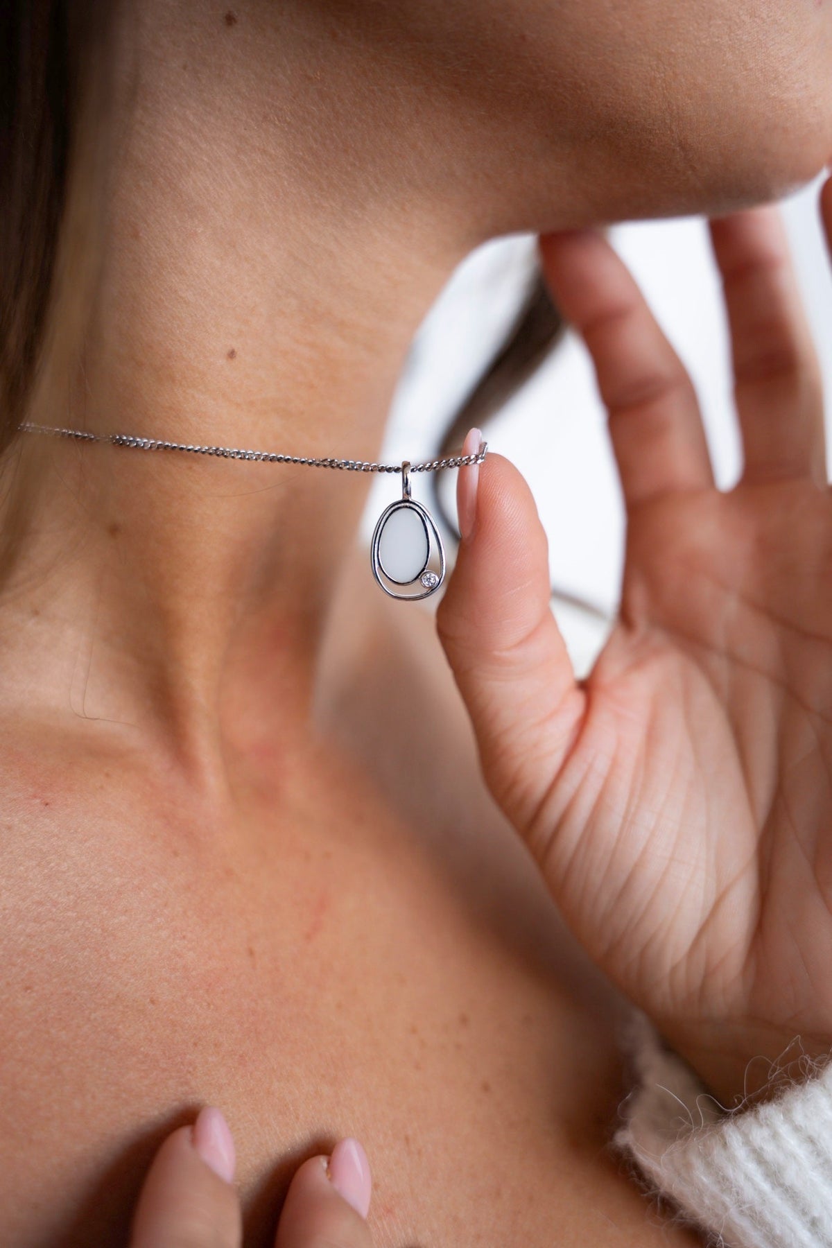 Fingers holding the Danique breast milk pendant in 925 sterling silver, with its free-flowing line around the stone.