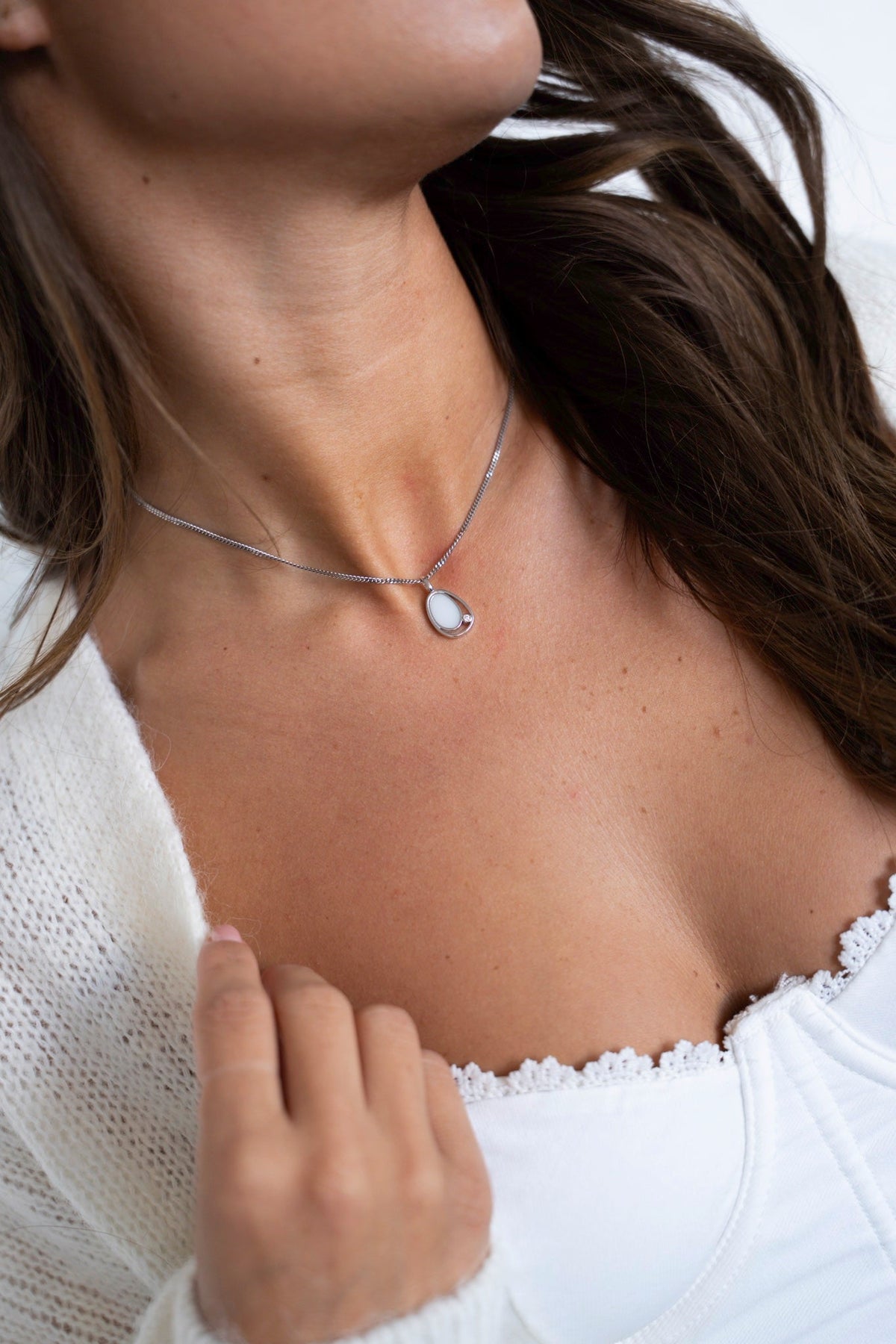 Woman in a white lace top wearing the Danique breast milk pendant in white gold.