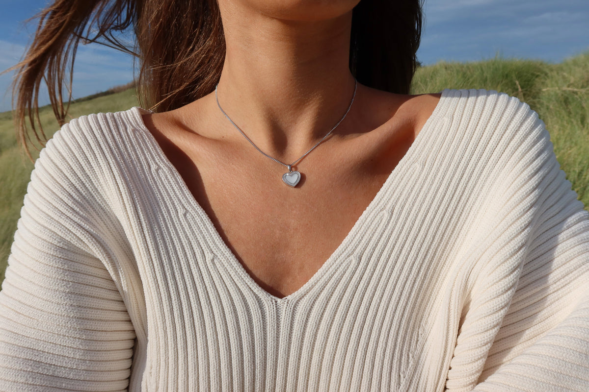 Close-up of the silver Demi heart breast milk pendant worn with a white V-neck sweater