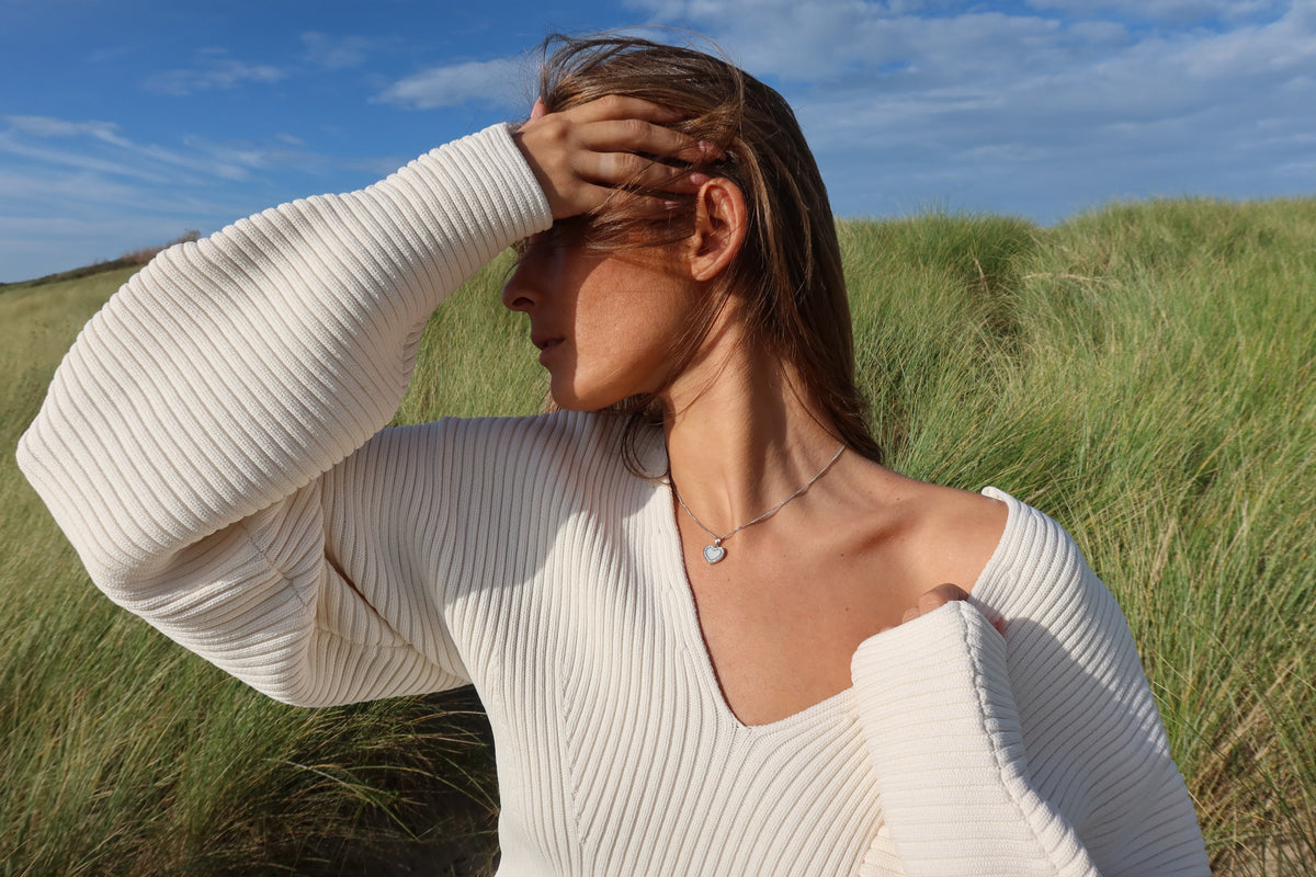 Woman in a white sweater in the dunes wearing the silver Demi heart breast milk pendant