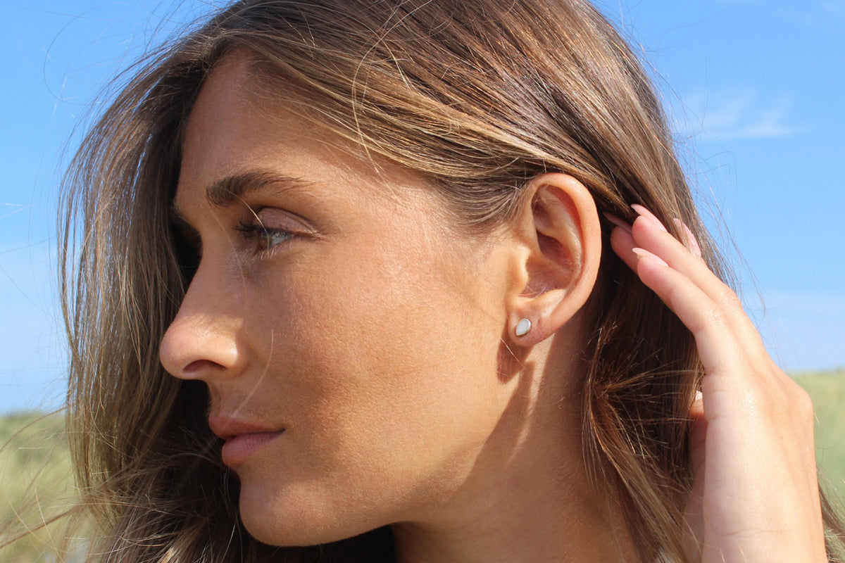 Woman in profile with her hand in her hair, wearing a silver Drop teardrop breast milk stud