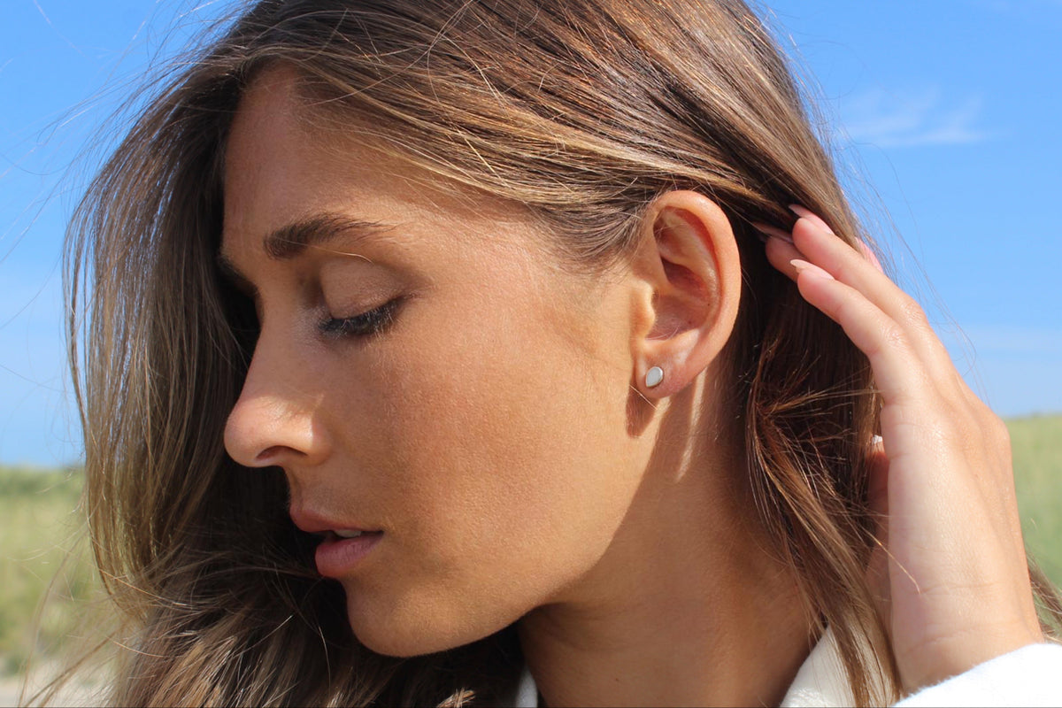 Woman looking down with her hand in her hair, wearing a silver Drop breast milk stud earring