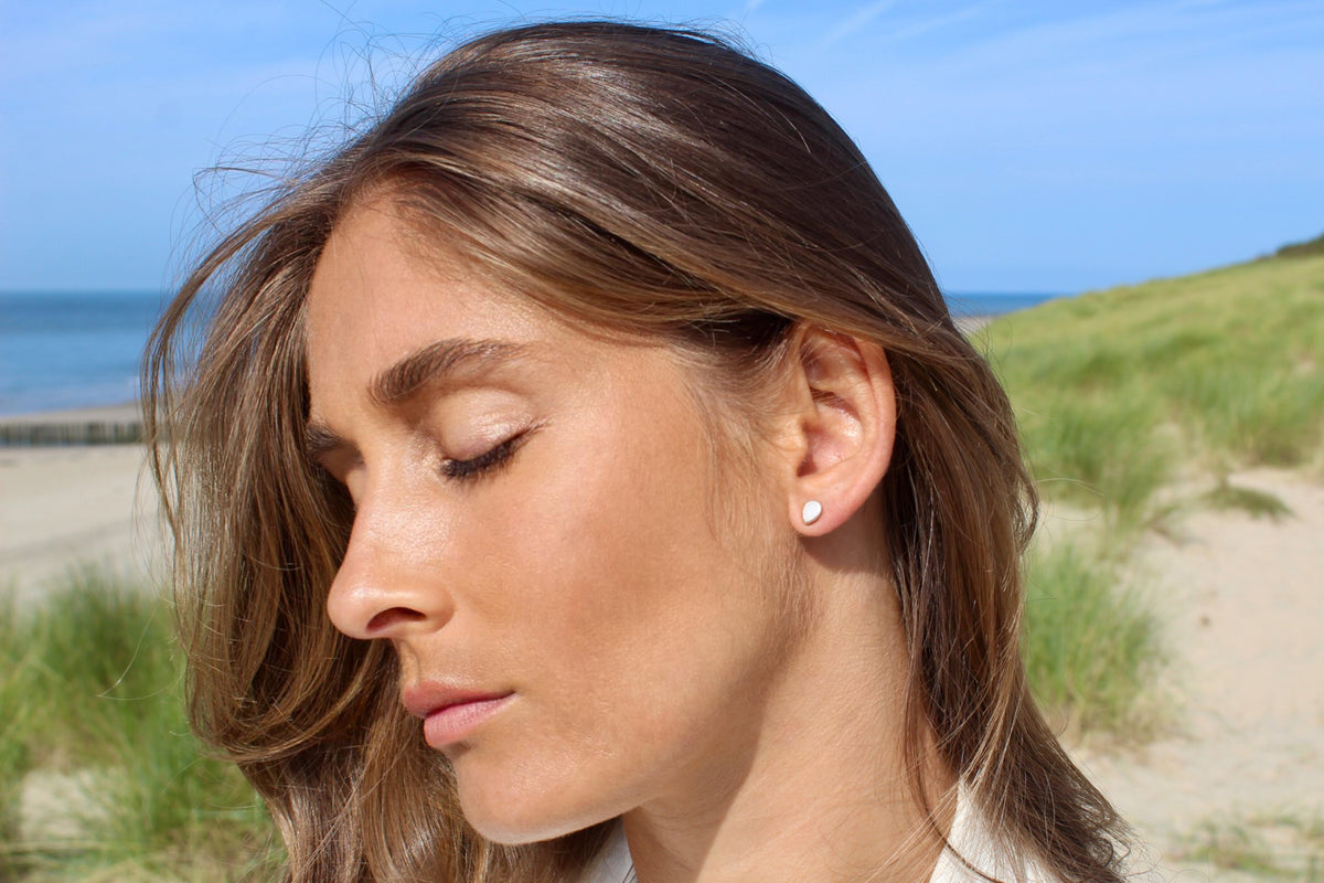 Woman with eyes closed in front of the sea, wearing a silver Drop teardrop breast milk stud