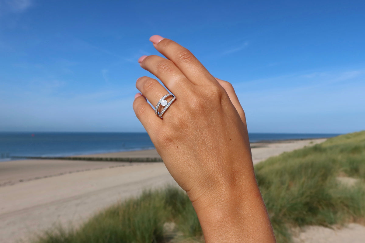 Hand against a blue sky wearing a silver split-band ring with a milk stone, a different model than Droplet