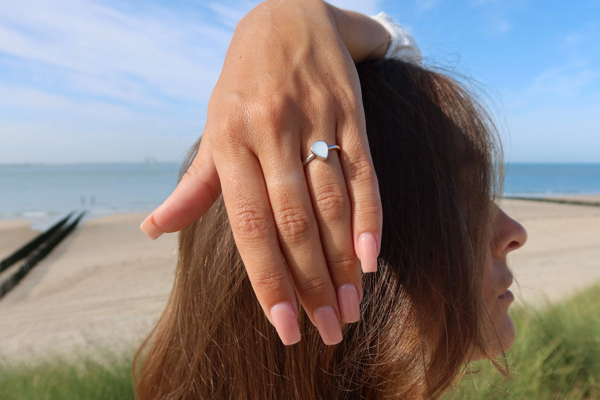 Hand resting on top of the head at the beach, wearing the silver teardrop Droplet breast milk ring