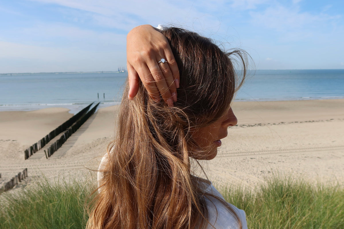 Woman holding her hair back at the beach, wearing the silver Droplet breast milk ring