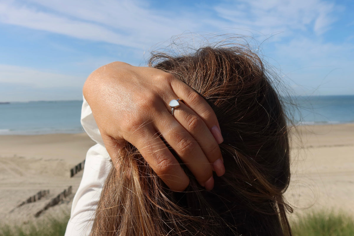 Hand gathering long hair at the beach, wearing the silver teardrop Droplet breast milk ring