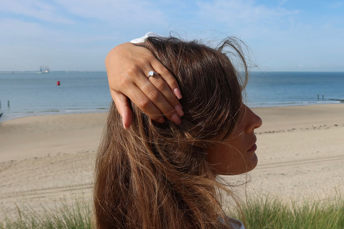 Woman in profile at the beach with her hand in her hair, wearing the silver Droplet breast milk ring