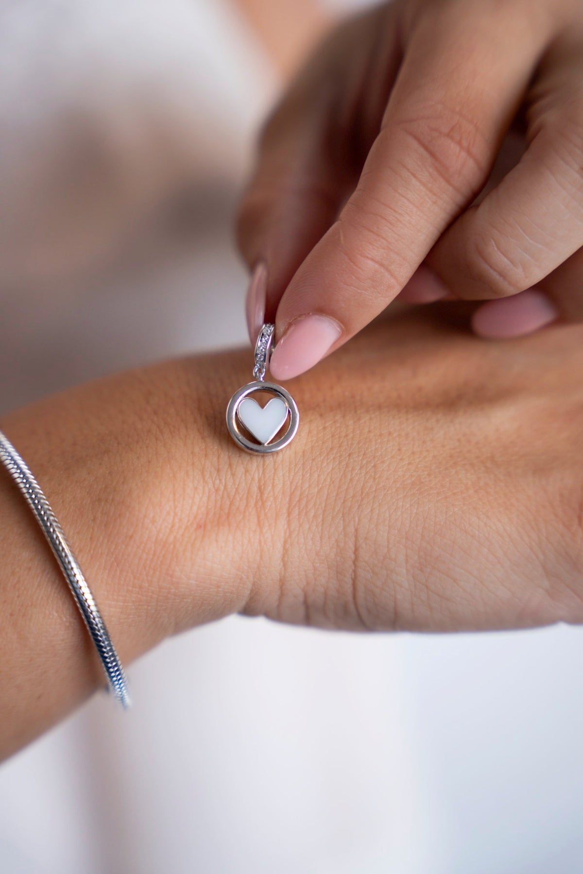 Silver Eline charm: a round medallion with a breast milk heart, held above the wrist.