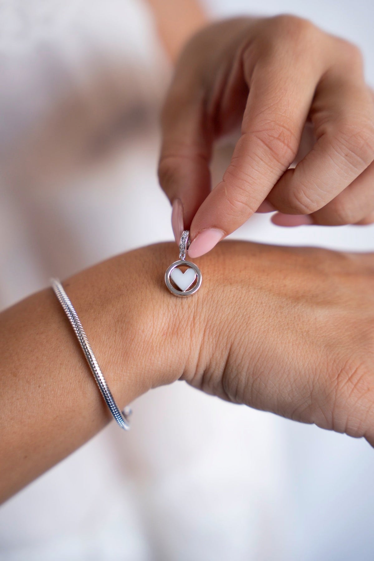Fingers holding the round white gold Eline charm with a breast milk heart above the hand.