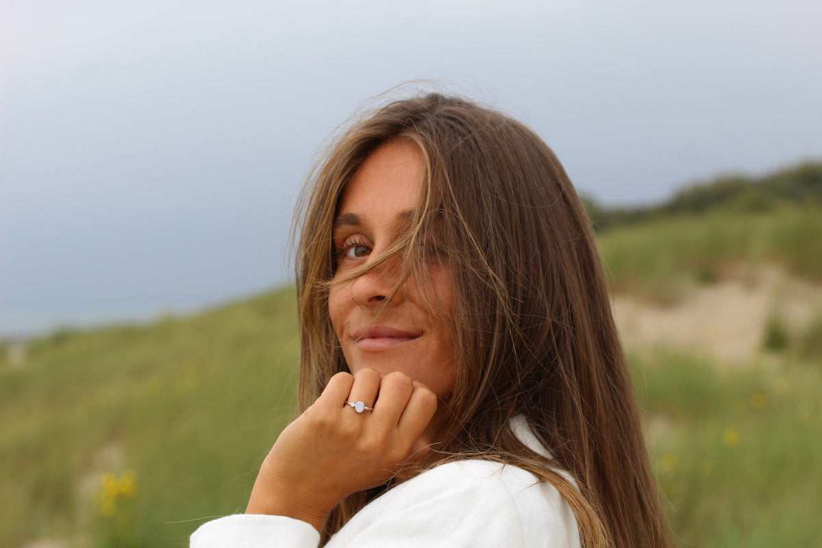 Smiling woman in the dunes with her hand at her chin, wearing the silver Elisa breast milk ring