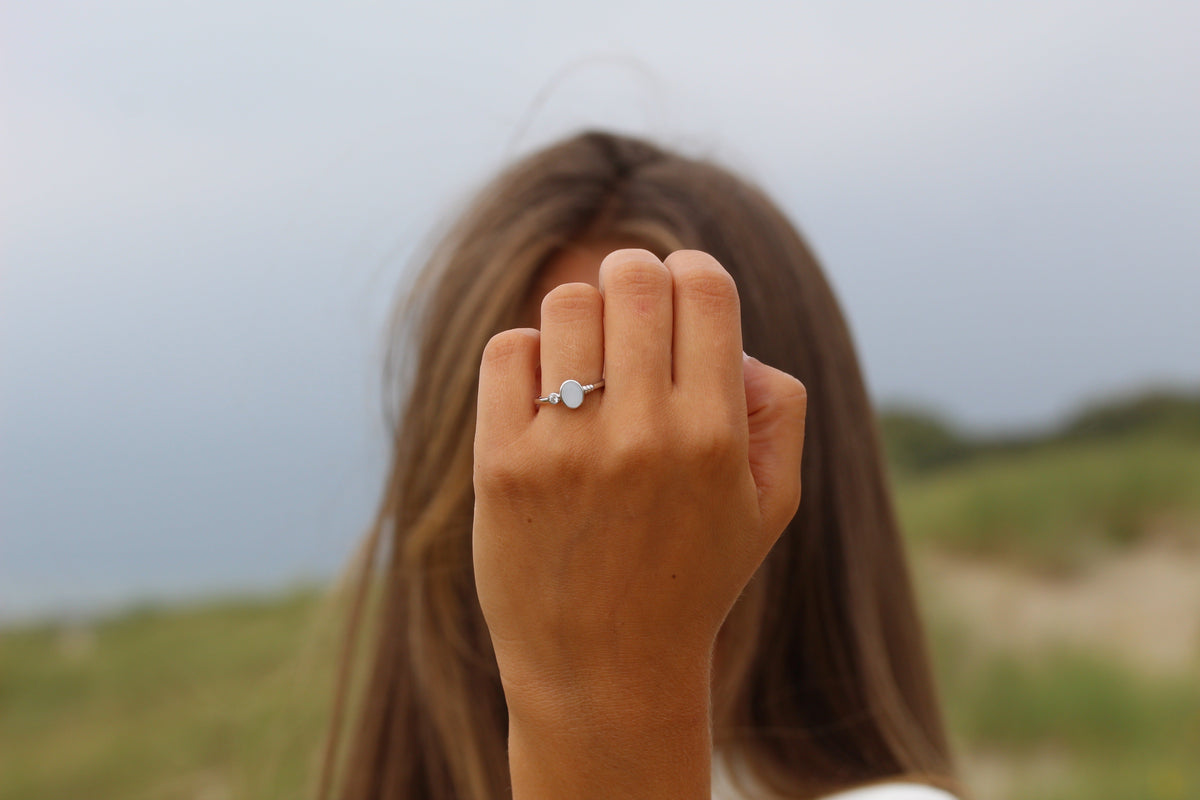 Raised fist in front of a face showing the silver-toned Elisa ring with an oval milk stone