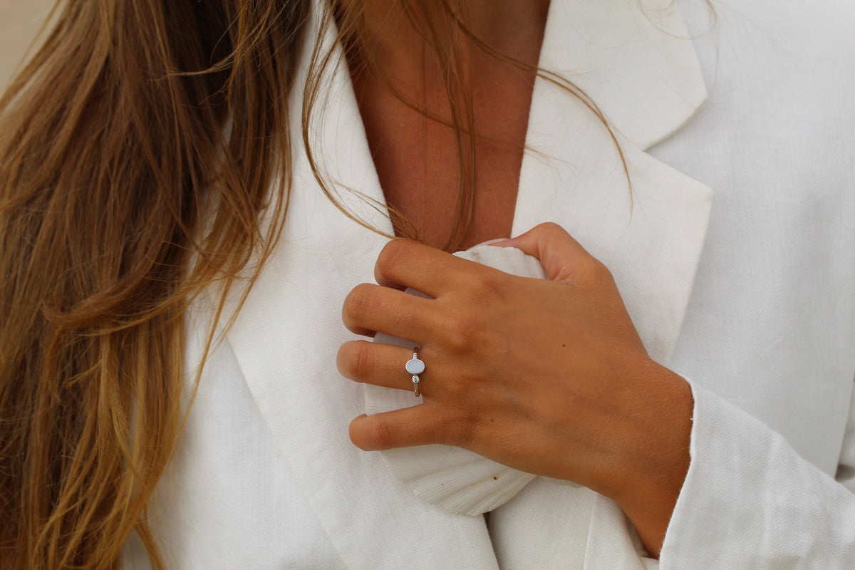 Hand holding a white shell against a linen blazer, wearing the silver-toned Elisa breast milk ring