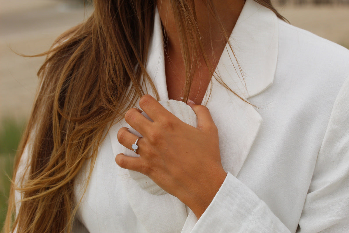 Close-up of a hand on a white blazer wearing the silver-toned Elisa ring with oval milk stone and side stone