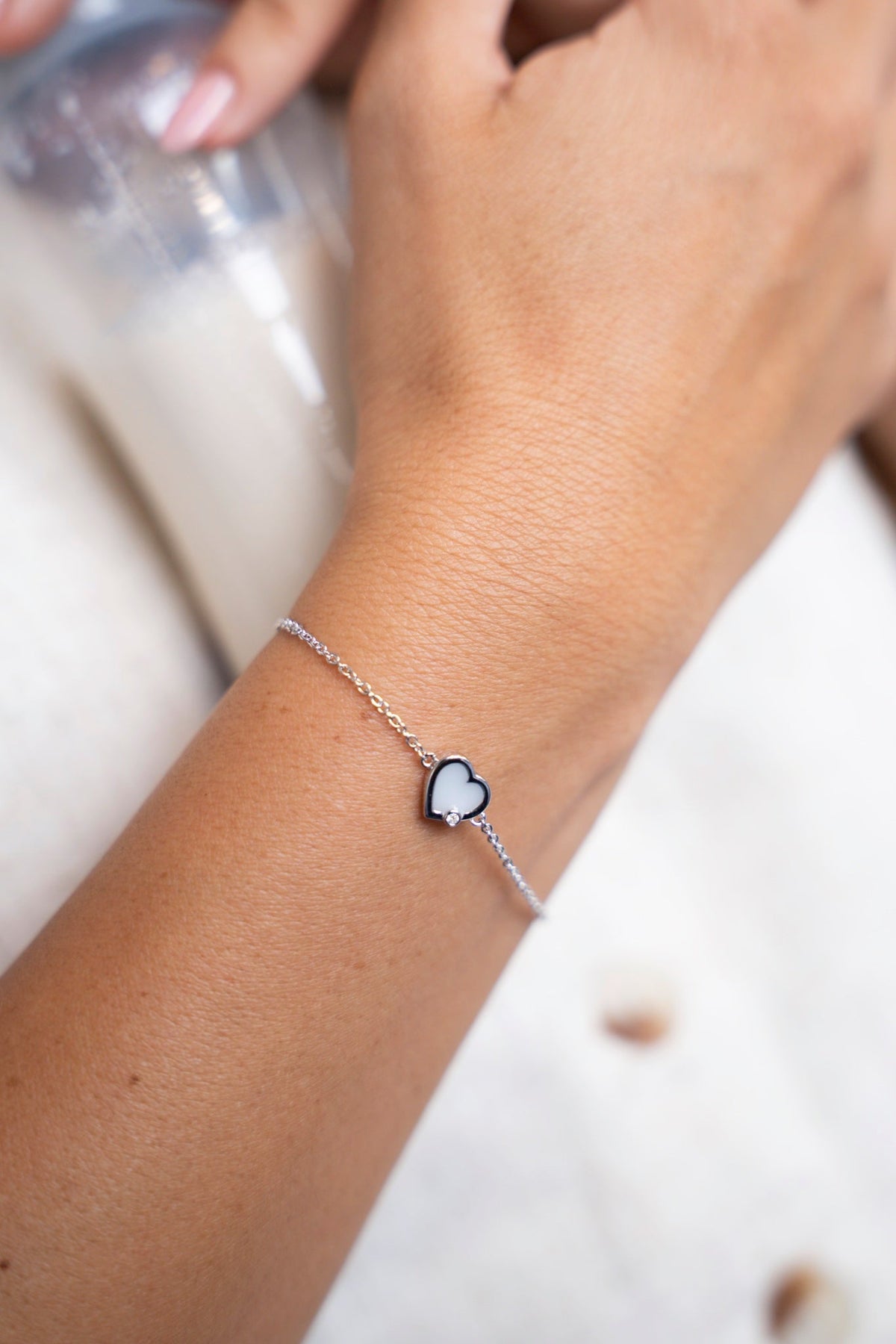 White gold Esmée bracelet with a heart-shaped breast milk stone on the wrist, next to a bottle of milk.