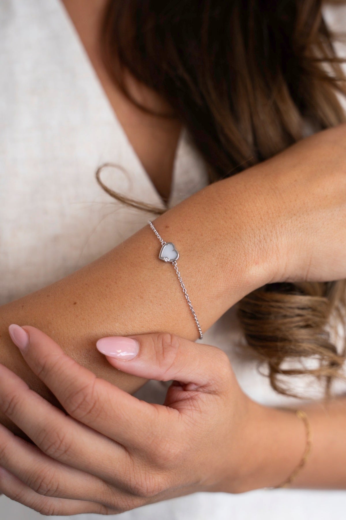 Esmée bracelet in solid white gold with a breast milk heart, worn on the wrist against a linen top.