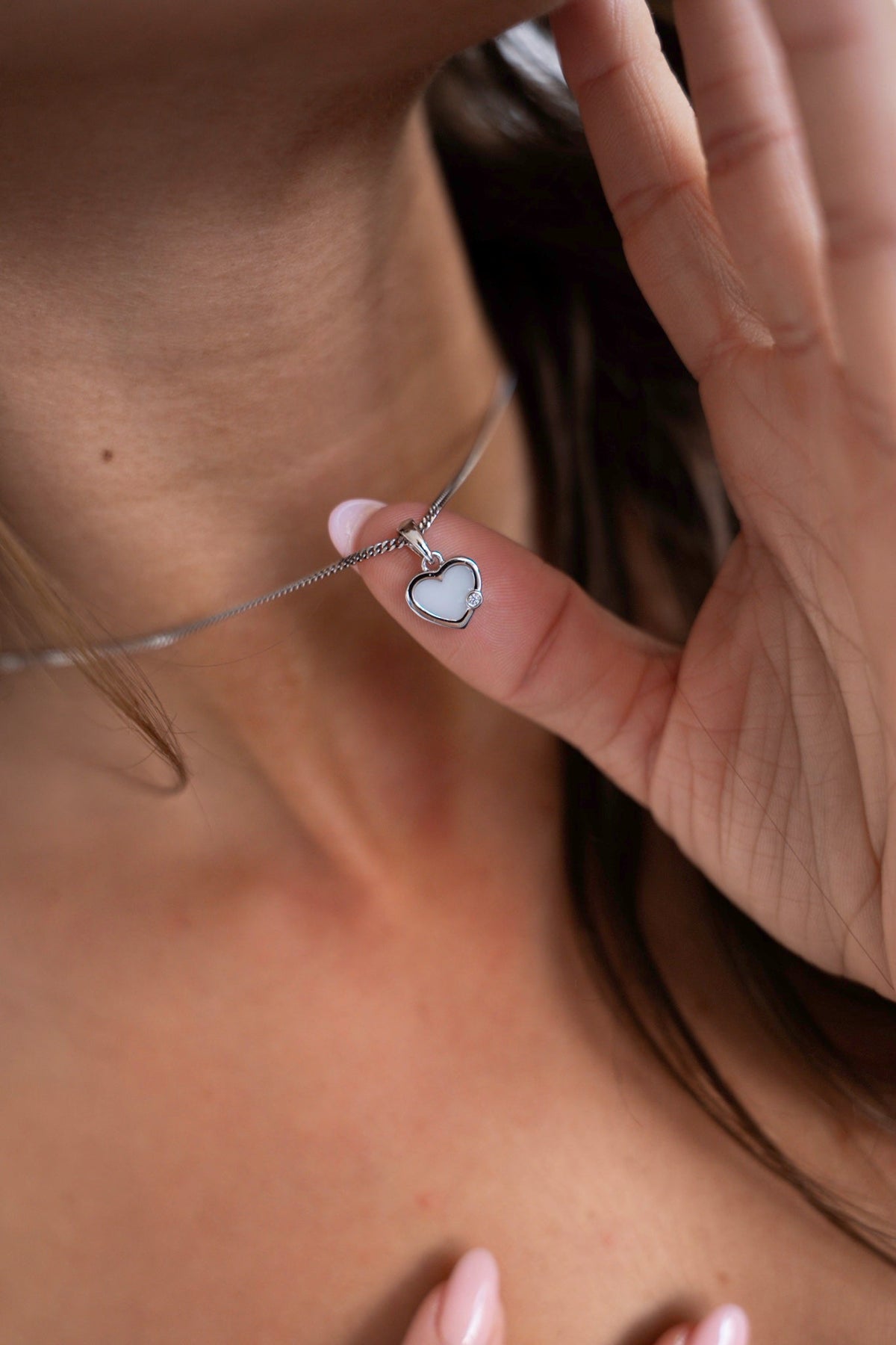 Fingers holding the heart-shaped Esmée pendant in silver with breast milk and a small stone.