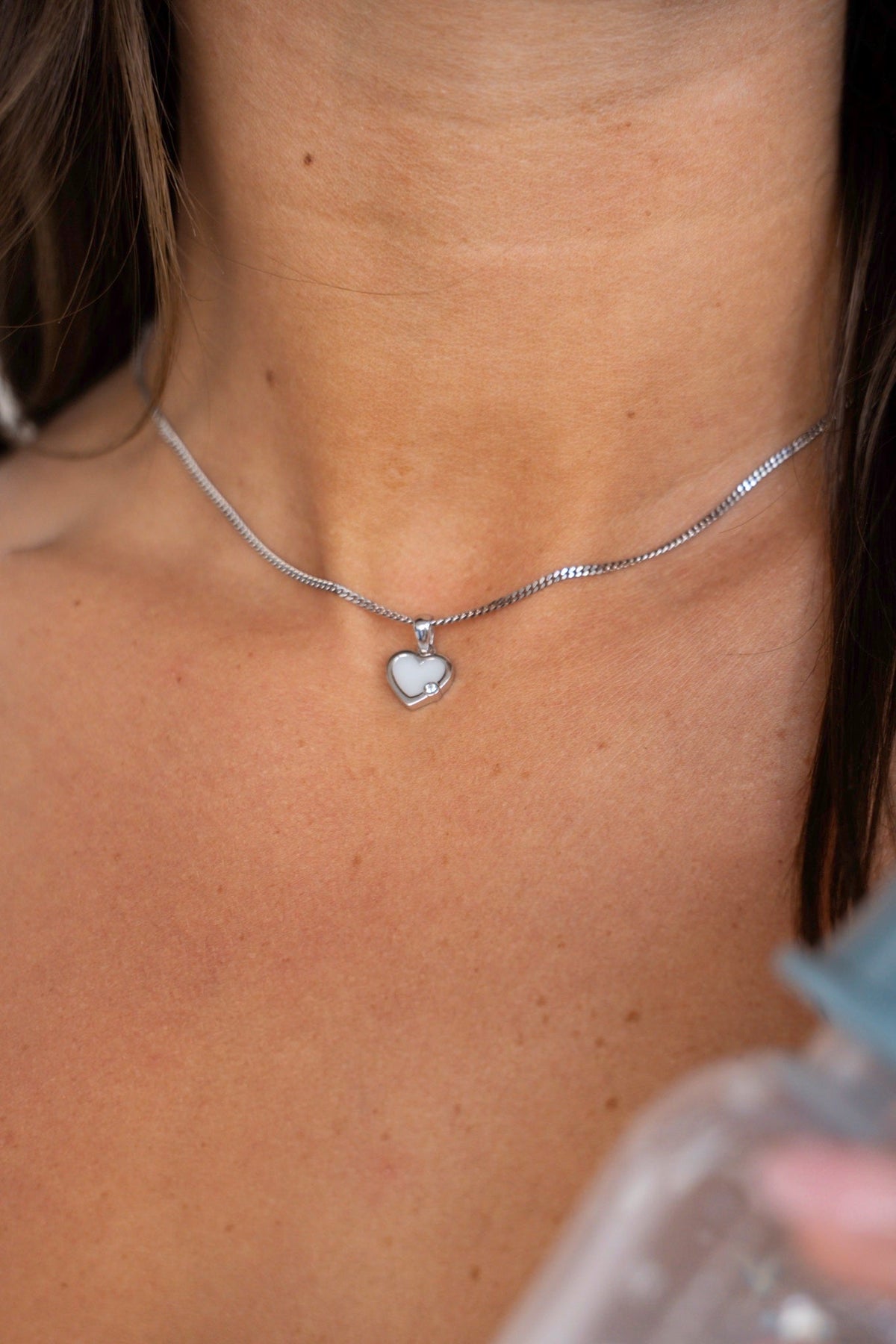 Close-up of the Esmée pendant in silver with a breast milk heart on the collarbone, next to a bottle of milk.