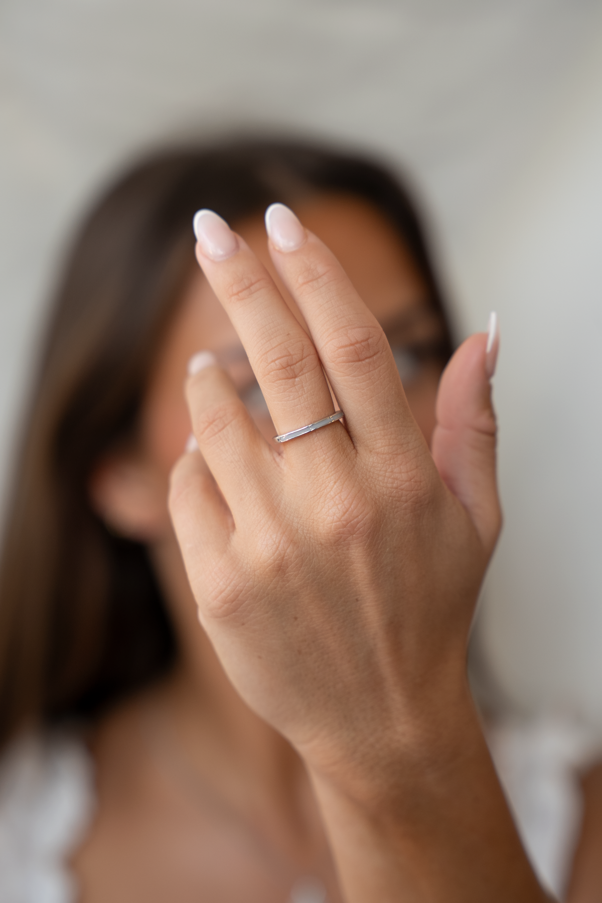 Raised hand in front of a face wearing the slim silver Eva breast milk band