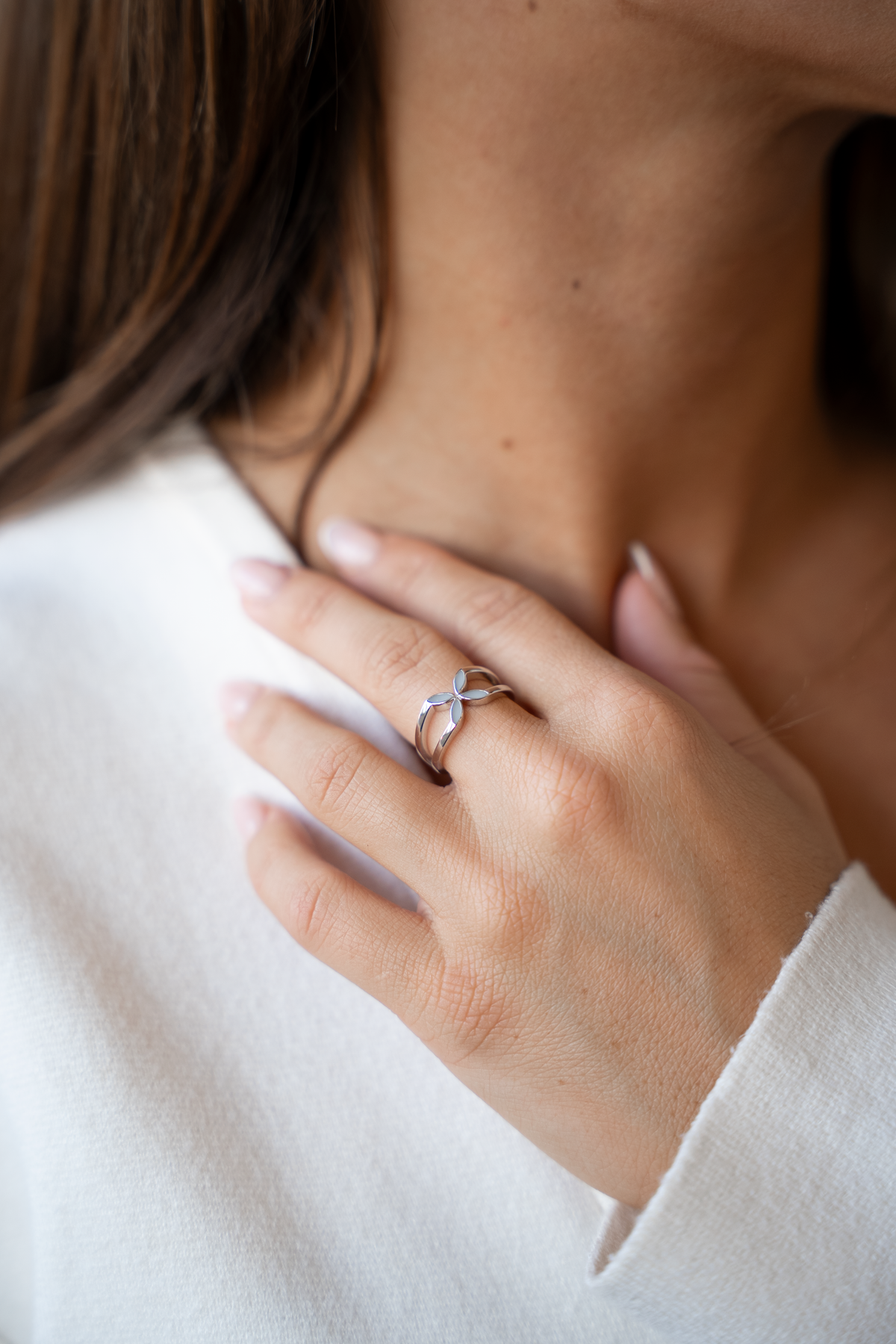 Hand resting at the neck wearing the silver Fleur ring with four milk-filled petals and split band