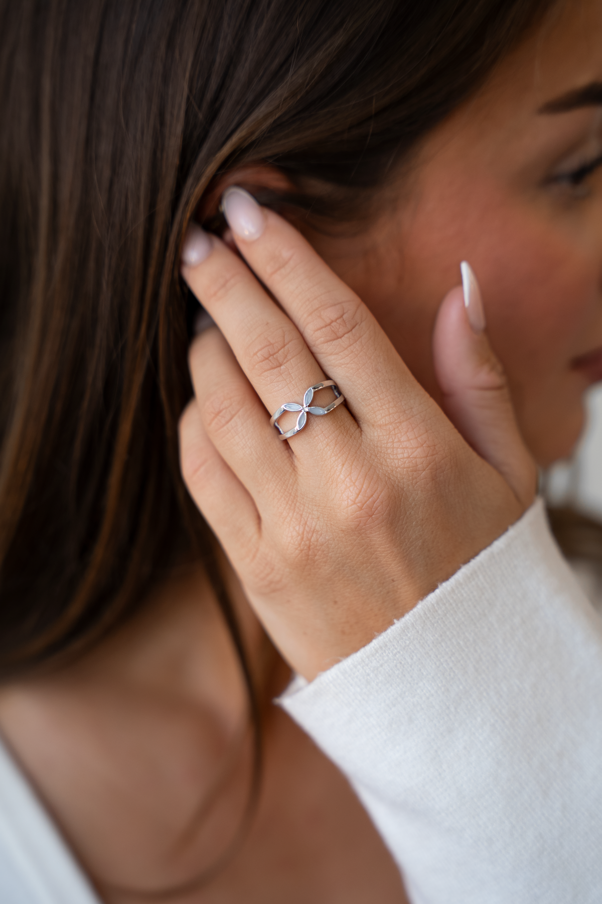 Close-up of a hand at the ear wearing the silver-toned Fleur breast milk ring with a flower of four petals