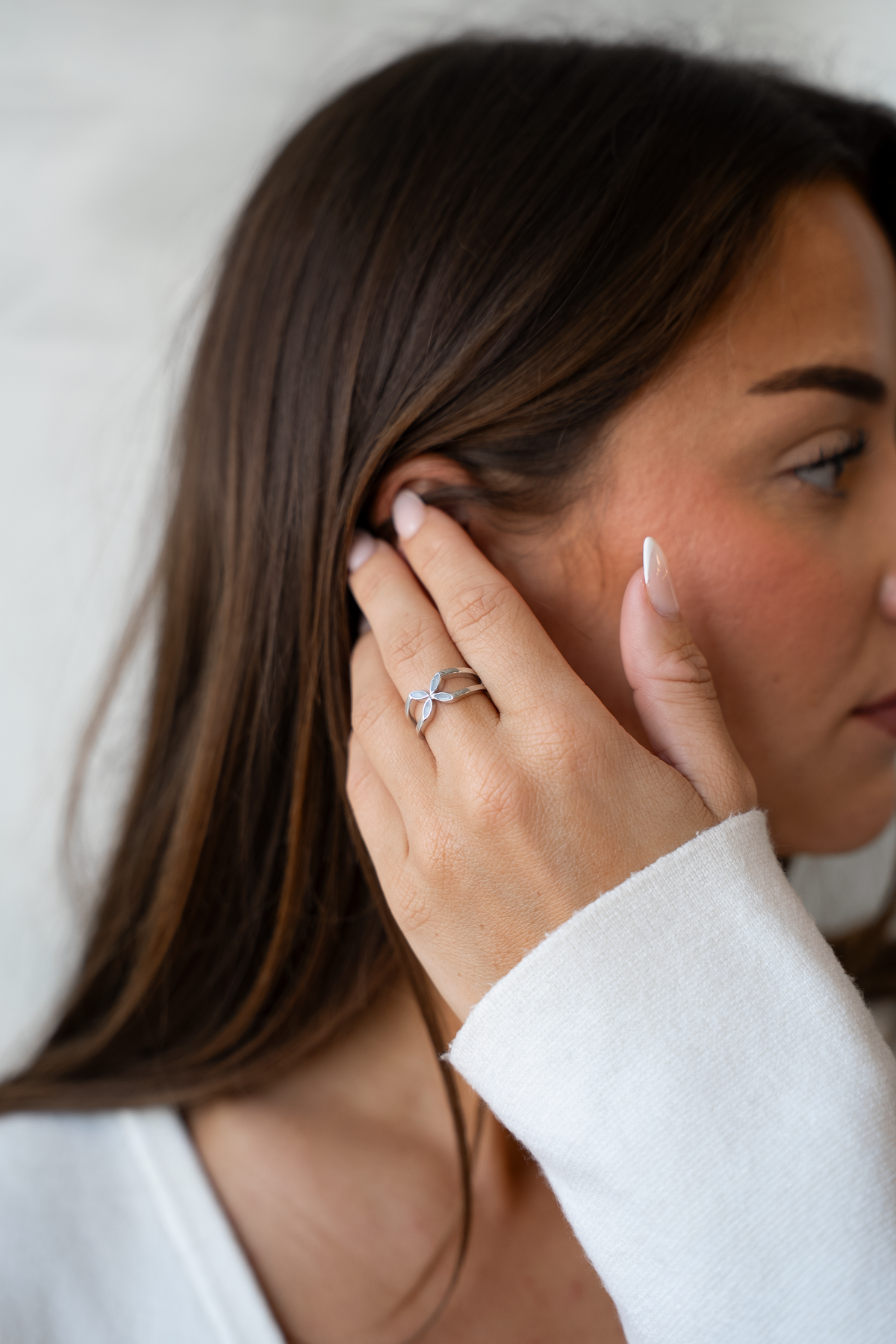 Woman tucking her hair behind her ear, wearing the silver-toned Fleur breast milk flower ring