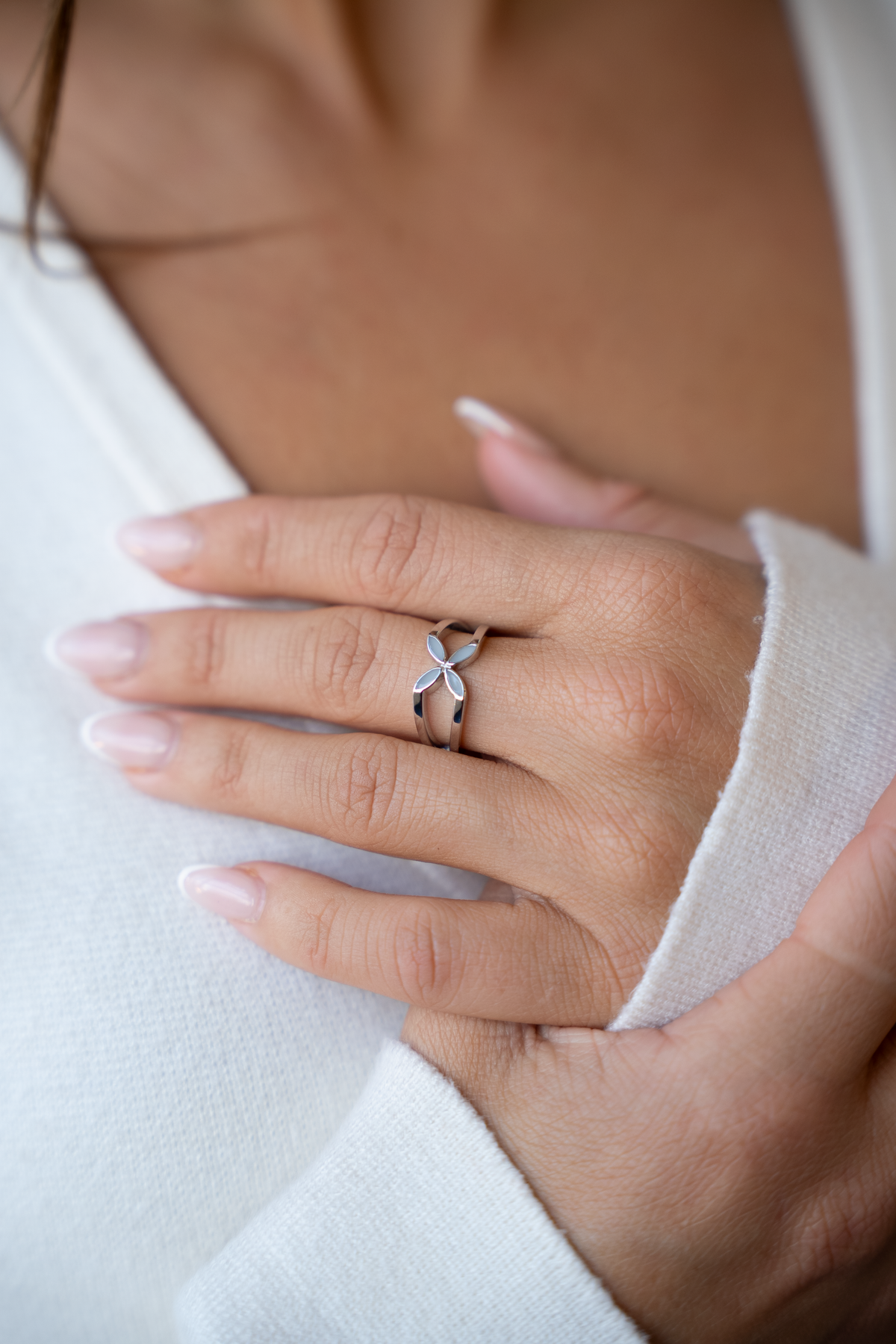 Hand on the chest over a white cardigan, wearing the silver-toned Fleur ring with four milk petals