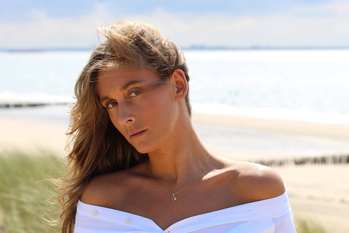 Woman on the beach wearing the Heart to Heart breast milk pendant in yellow gold on a fine chain