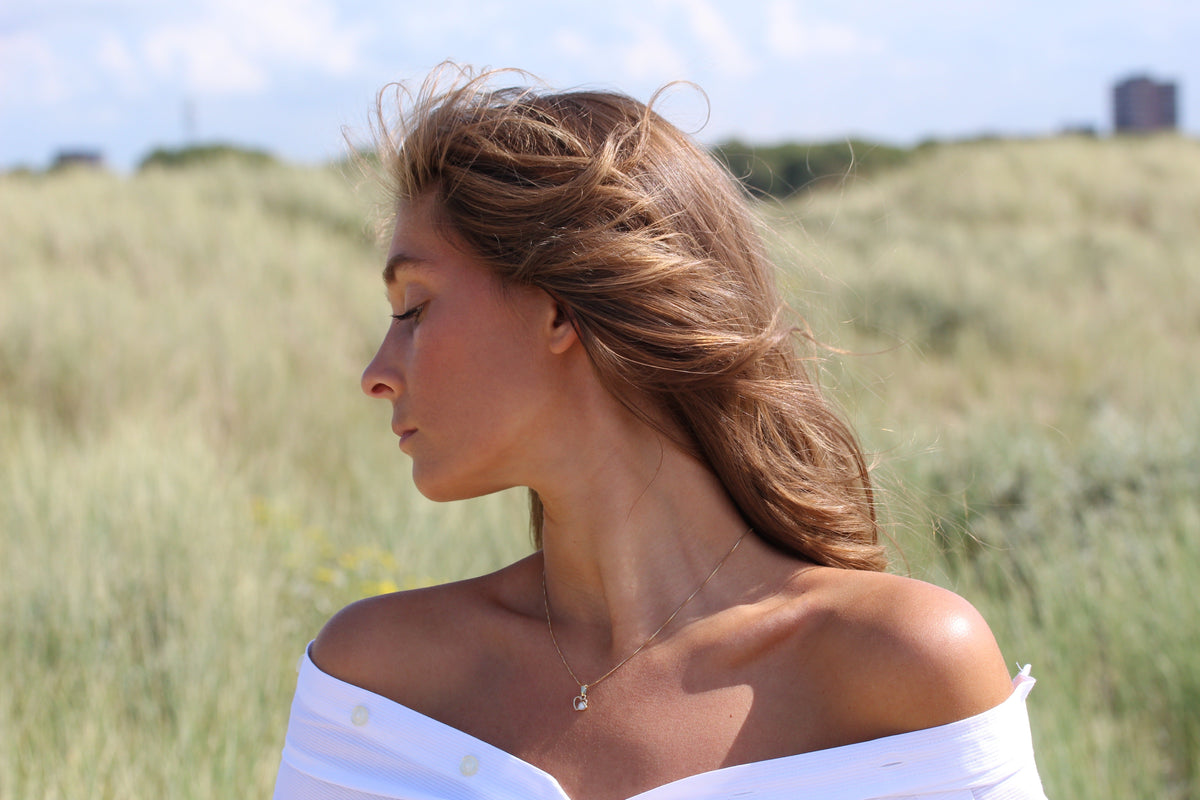 Woman in the dunes looking down, wearing the Heart to Heart breast milk pendant in yellow gold