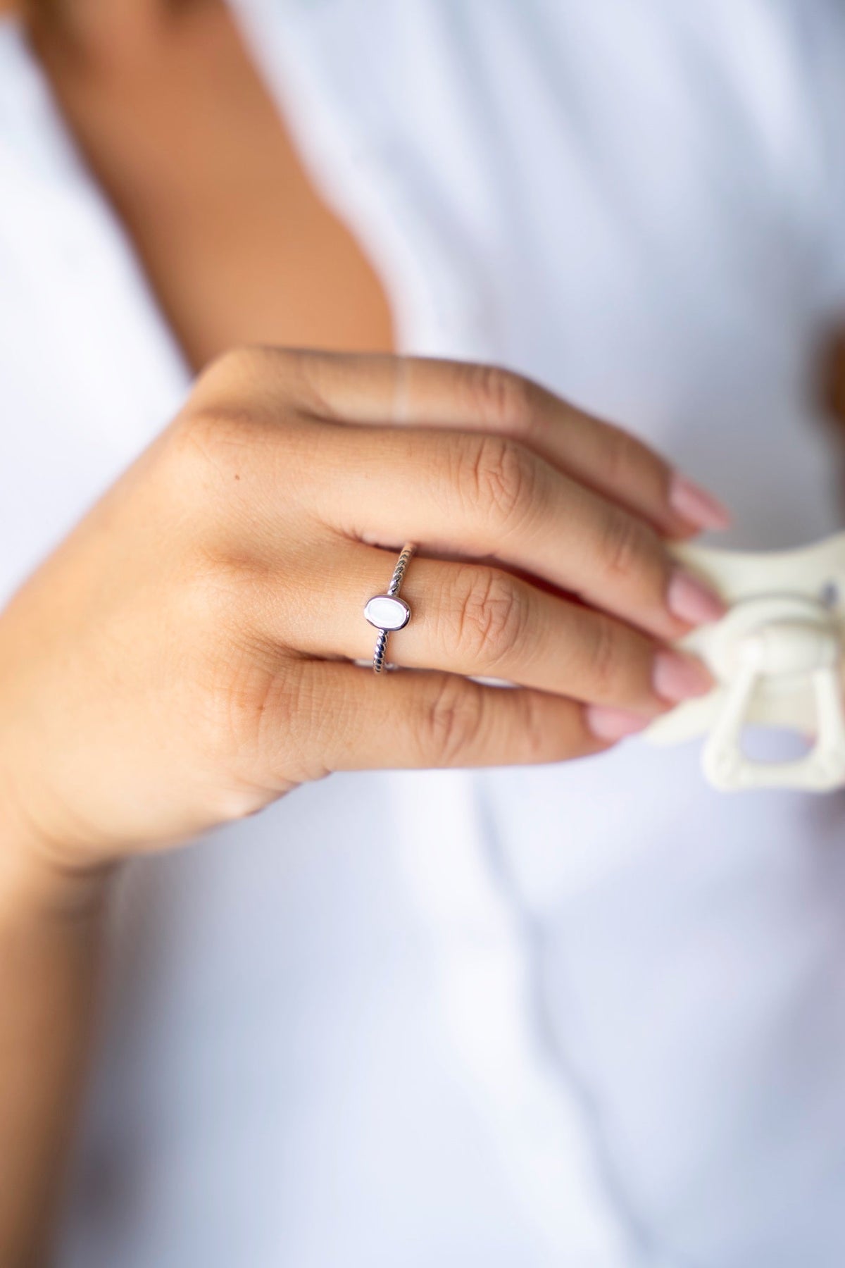 Silver Ilse ring with an oval breast milk stone and detailed band, holding a pacifier.