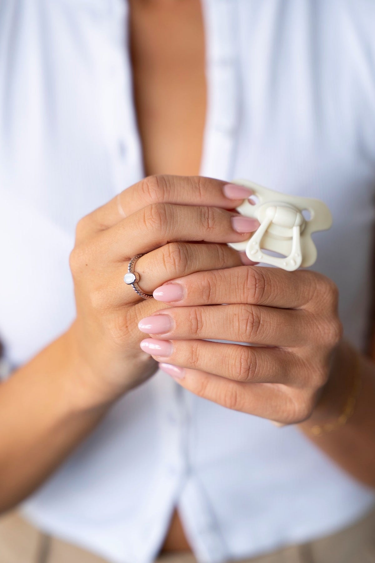 Hands holding a white pacifier, with the Ilse breast milk ring in solid white gold on the finger.