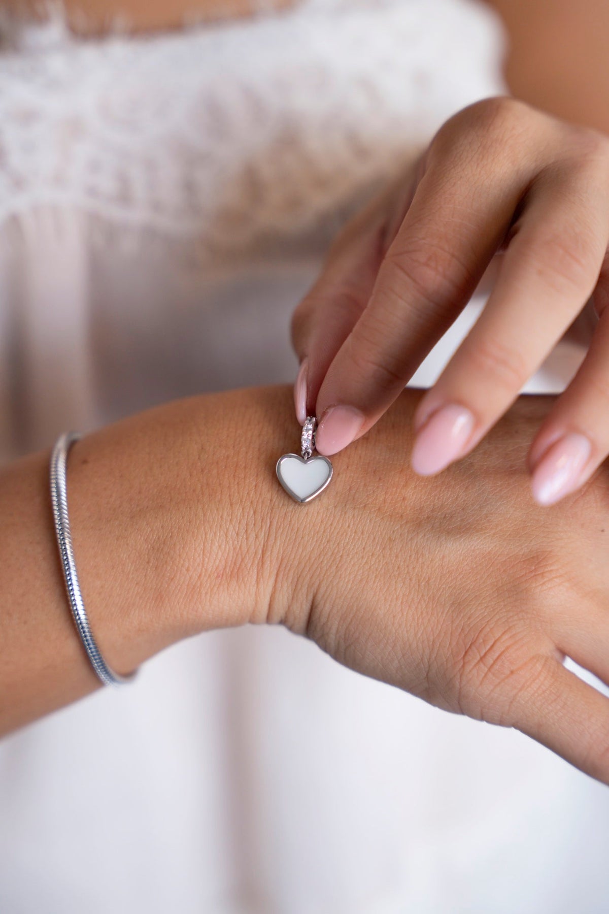 Silver Indy breast milk charm held above the hand, next to a bracelet.