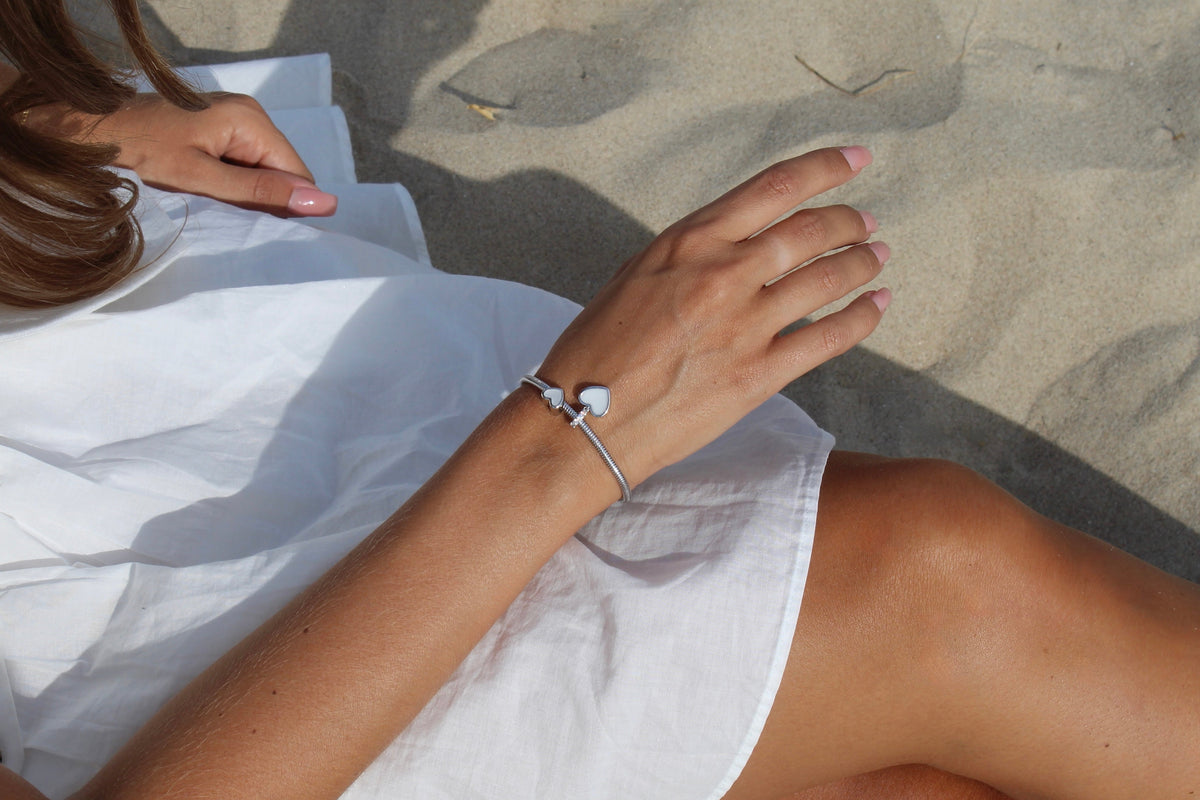 Woman in a white dress on the beach wearing a silver bracelet with the Indy heart breast milk charm