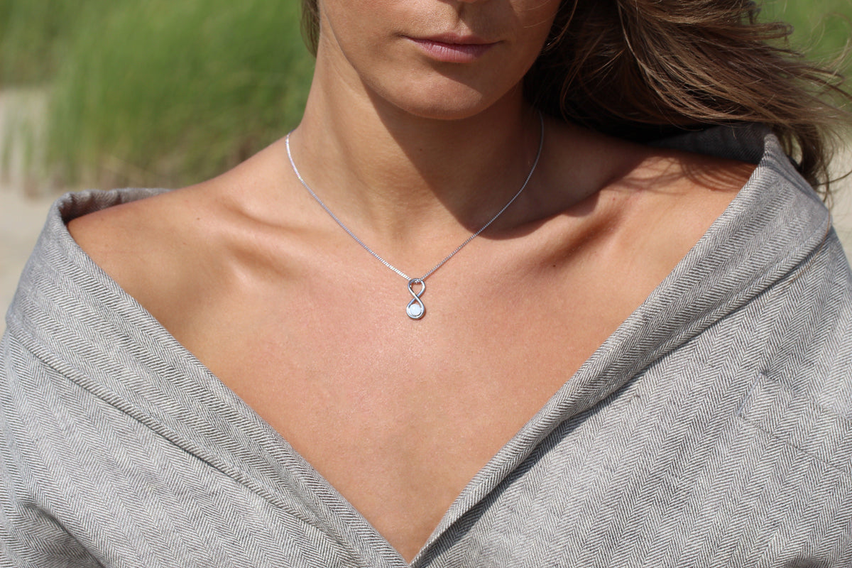 Close-up of a woman in a gray linen blazer wearing the silver Infinity breast milk pendant