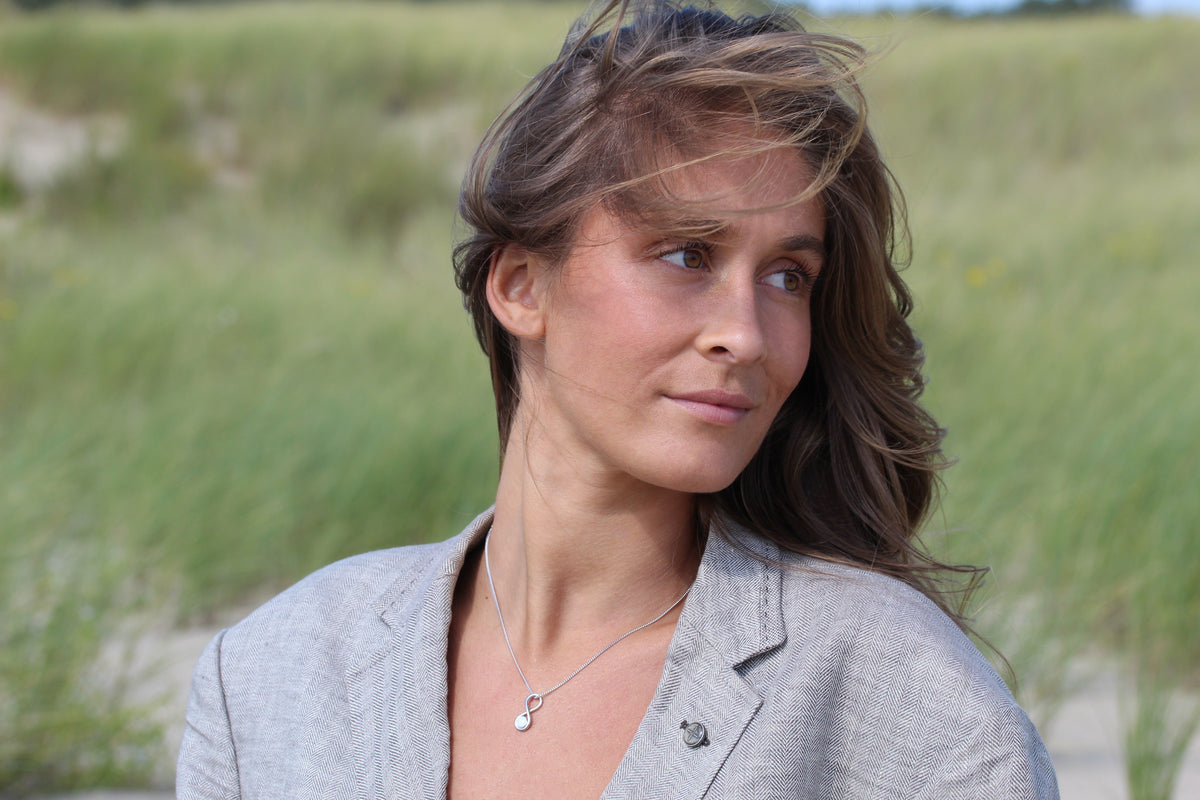 Woman in a gray blazer in the dunes wearing the silver-tone Infinity breast milk pendant on a chain
