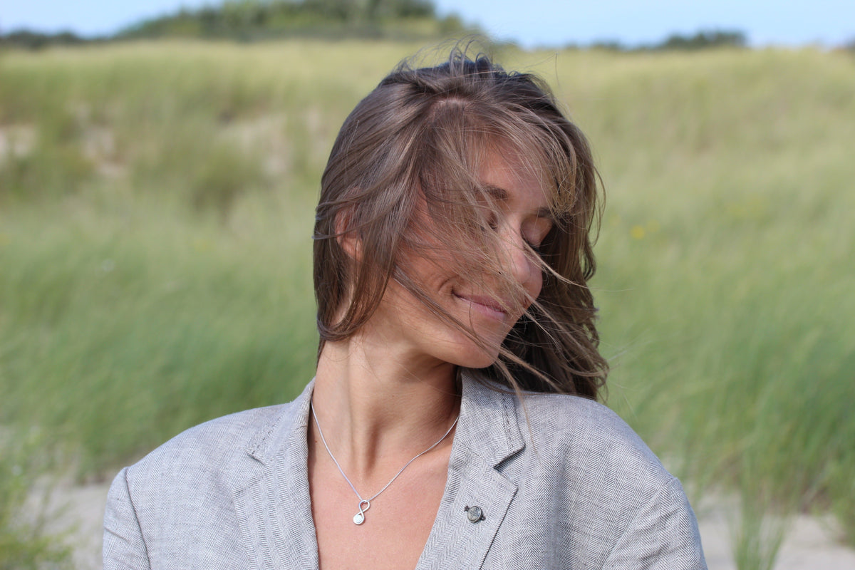 Woman with hair blowing across her face wearing the silver-tone Infinity breast milk pendant