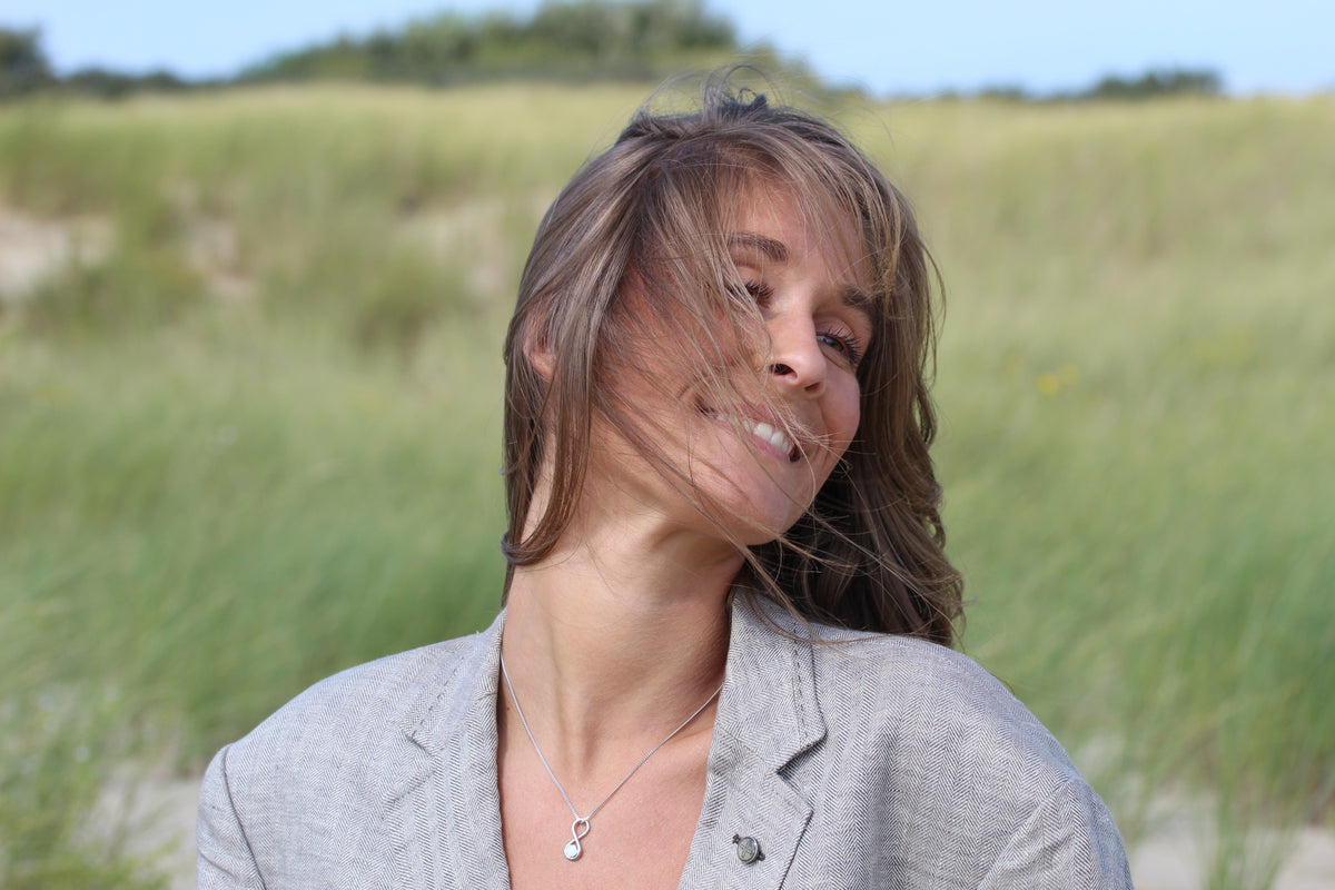 Laughing woman in the dunes wearing the silver-tone Infinity breast milk pendant on a fine chain