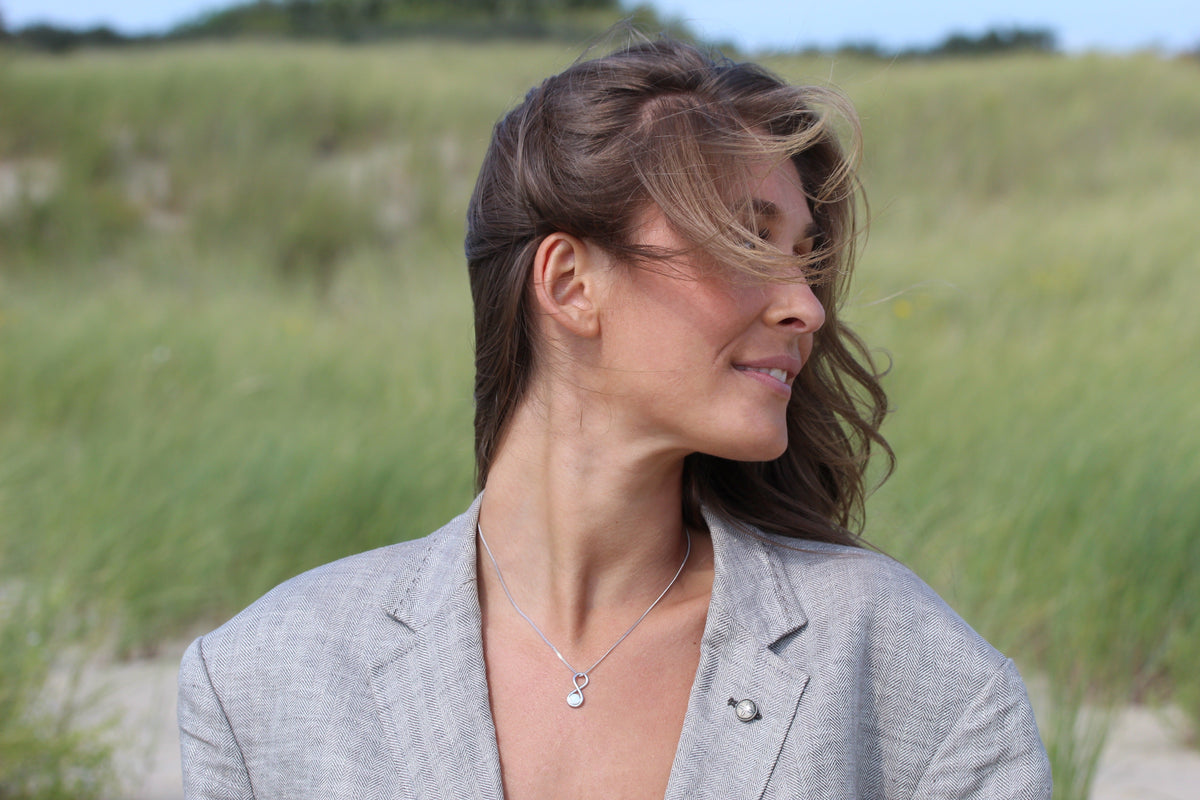 Woman in the dunes looking to the side wearing the silver-tone Infinity breast milk pendant