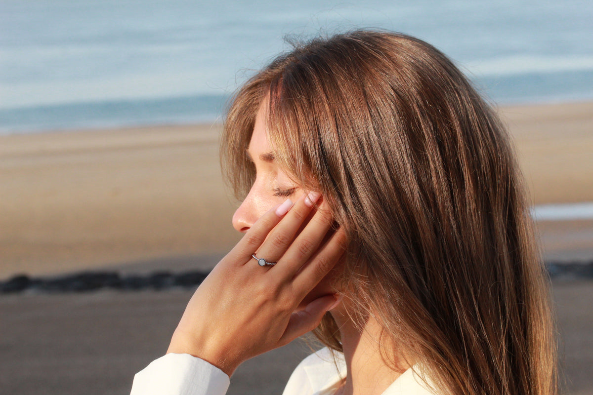 Woman in profile at the beach with a hand on her cheek, wearing the silver Isabelle breast milk ring