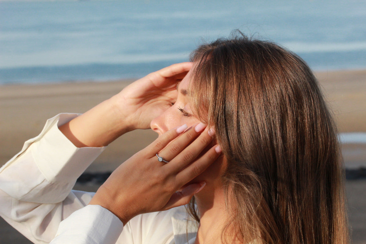 Woman shading her eyes at the beach, wearing the silver Isabelle ring with a round milk stone