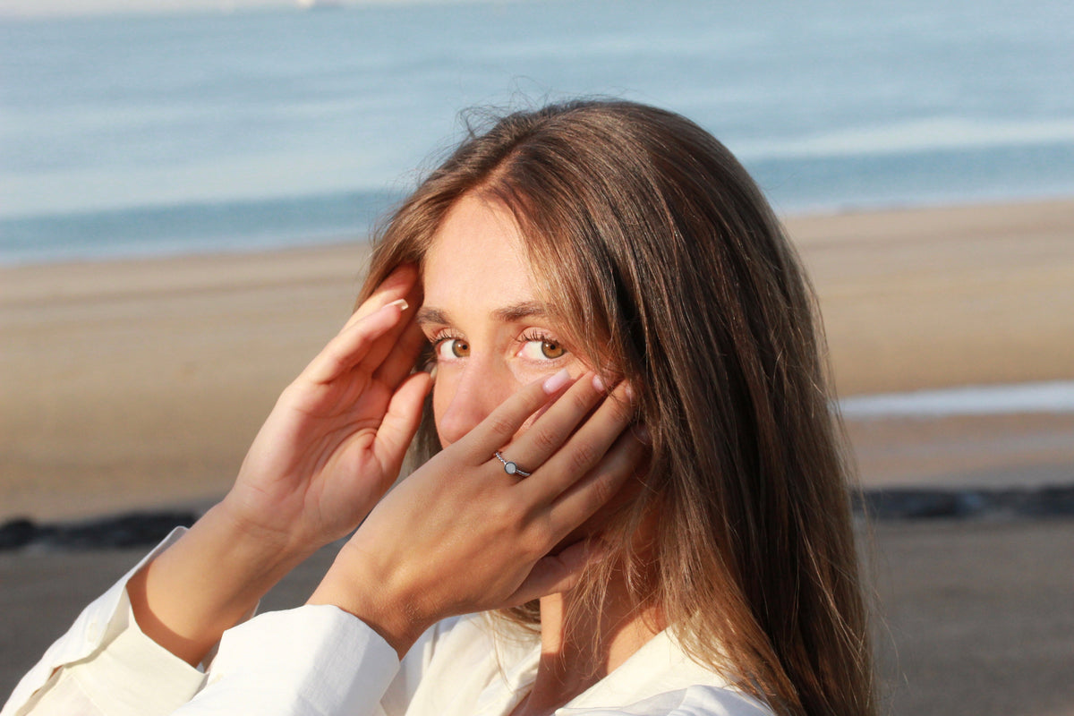 Woman framing her face with both hands at the beach, wearing the silver Isabelle breast milk ring