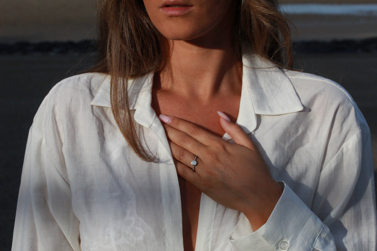 Hand on the chest over a white linen shirt, wearing the silver Isabelle breast milk ring