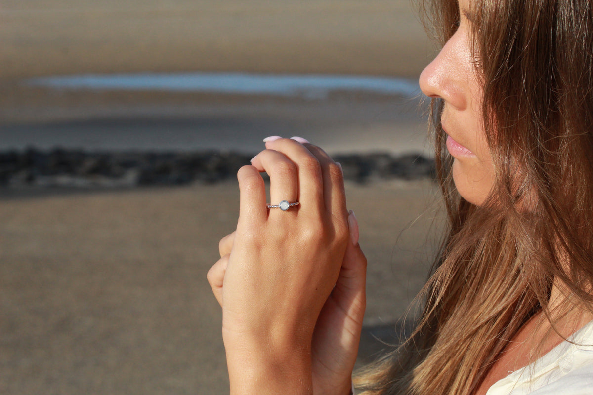 Woman at the beach with hands folded at her lips, wearing the silver-toned Isabelle breast milk ring