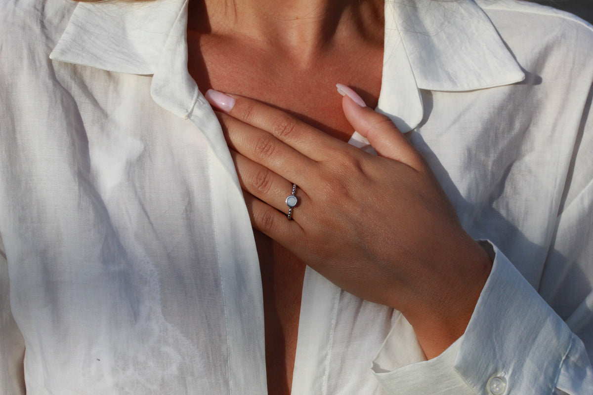 Close-up of a hand on a white shirt wearing the beaded silver-toned Isabelle ring with a round milk stone