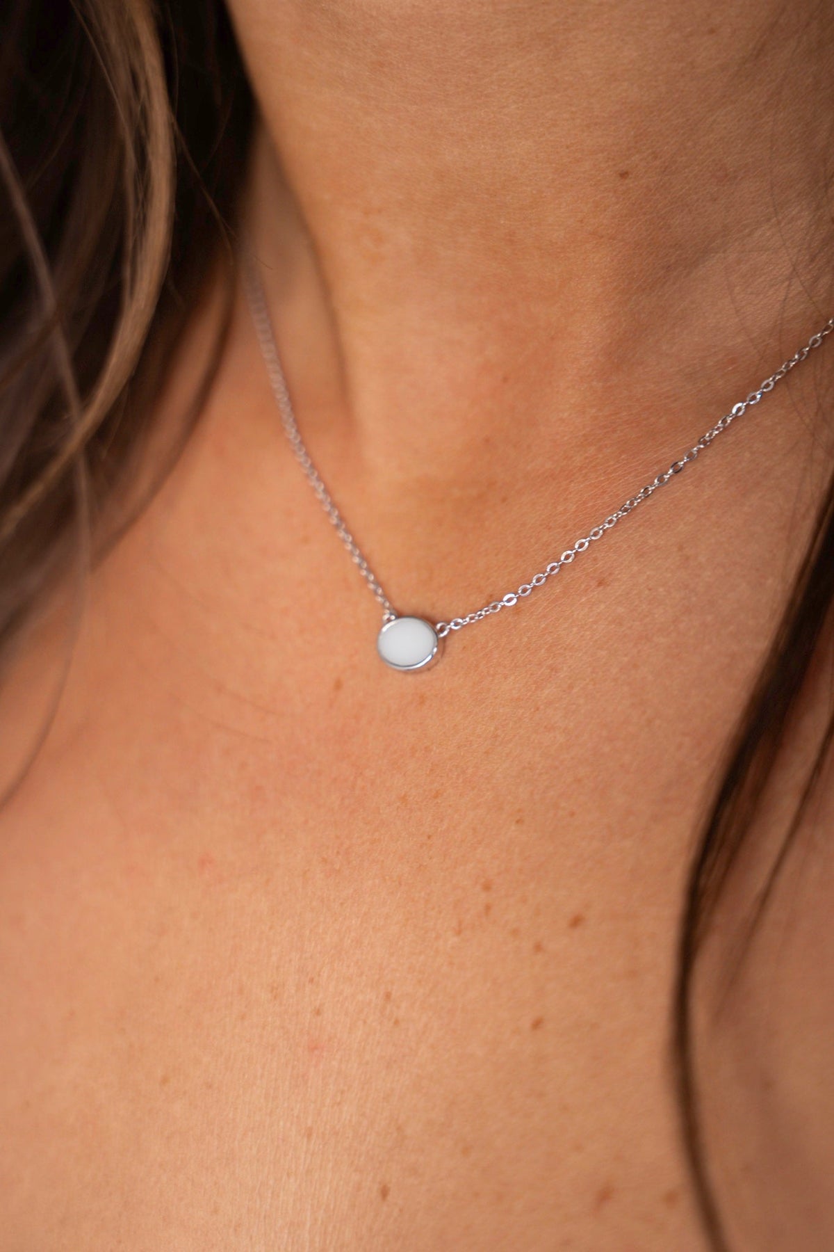 Close-up of the Juna breast milk necklace in solid white gold with faceted links and a smooth oval stone.