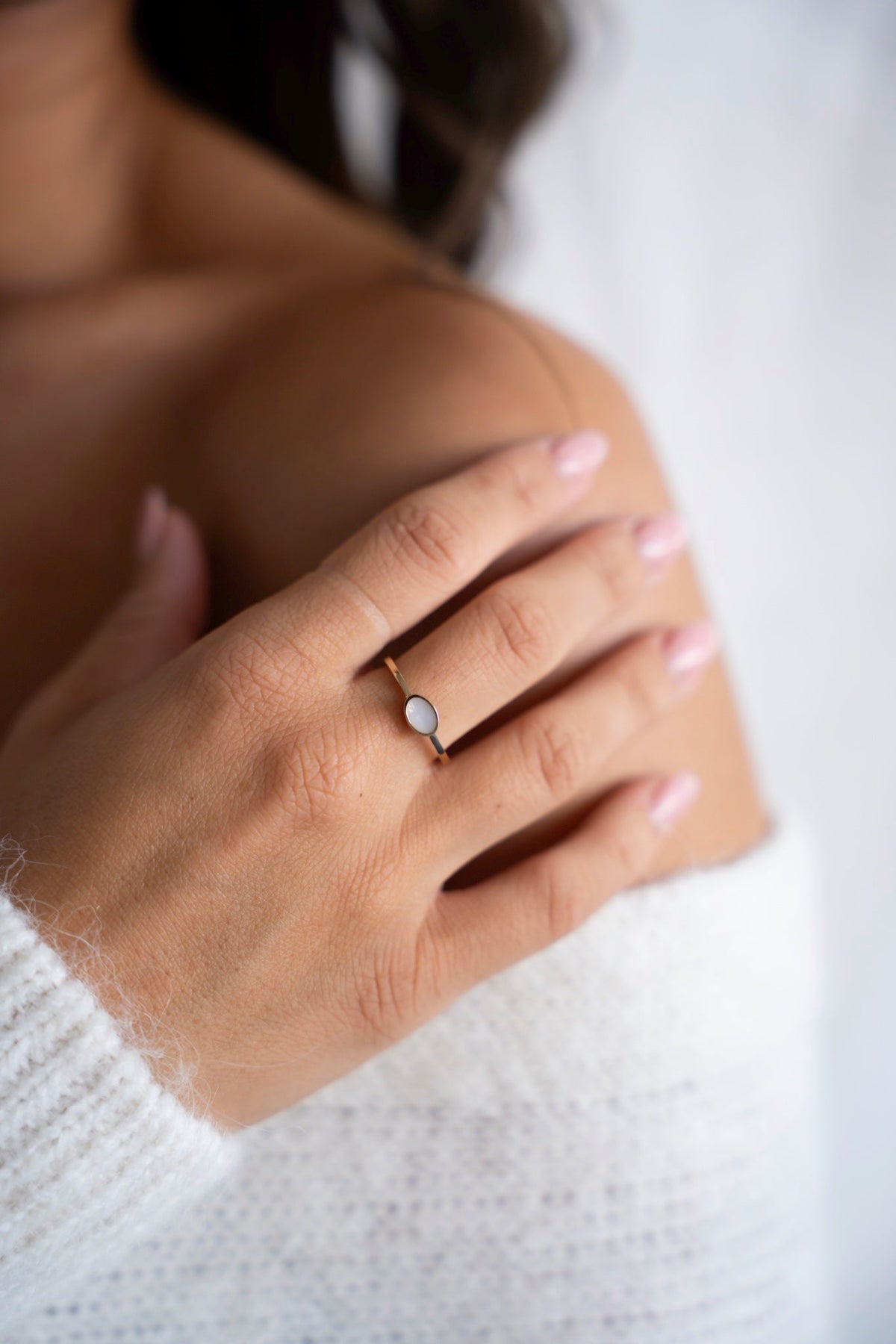 Hand on the shoulder wearing the gold Juna ring with an oval breast milk stone.
