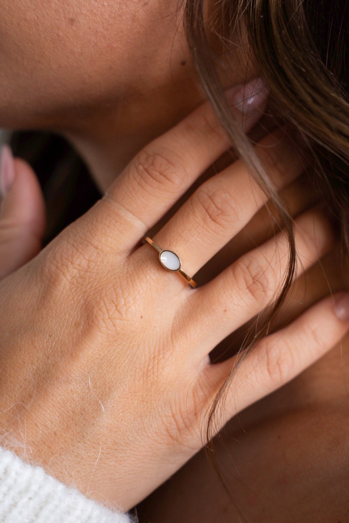 Close-up of the Juna ring in solid yellow gold with an oval breast milk stone, hand near the neck.